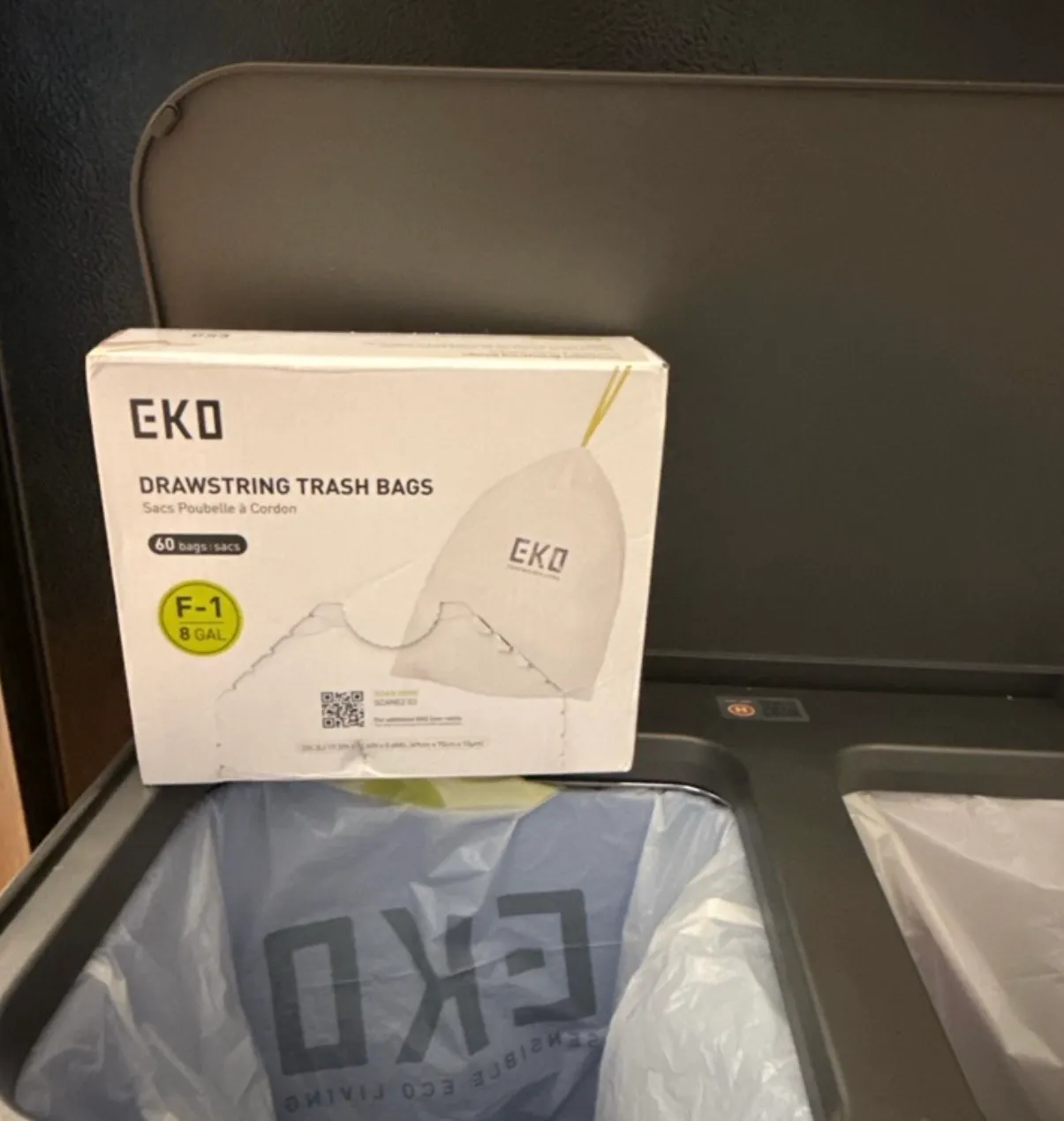 Box of EKO drawstring trash bags propped against a kitchen trash bin with a bag fitted inside