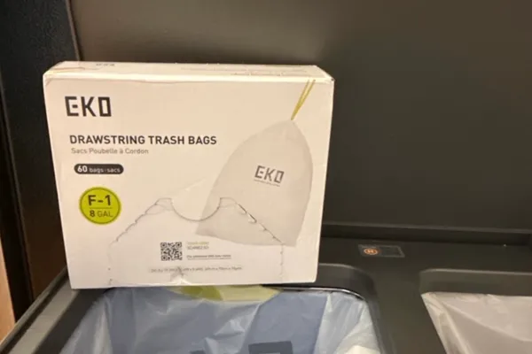 Box of EKO drawstring trash bags propped against a kitchen trash bin with a bag fitted inside